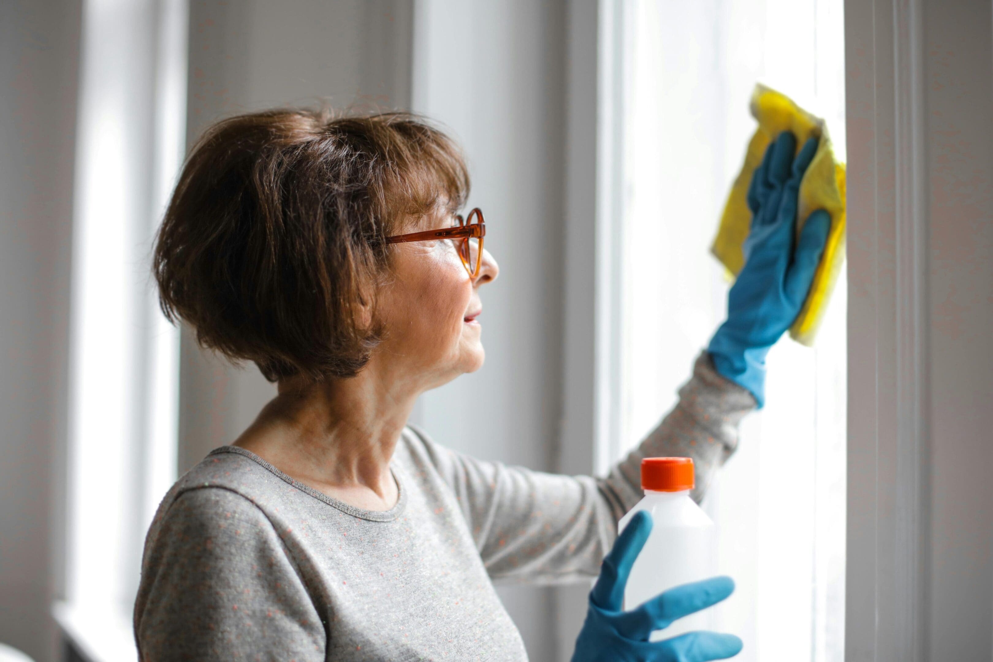A woman in glasses and gloves cleaning windows.